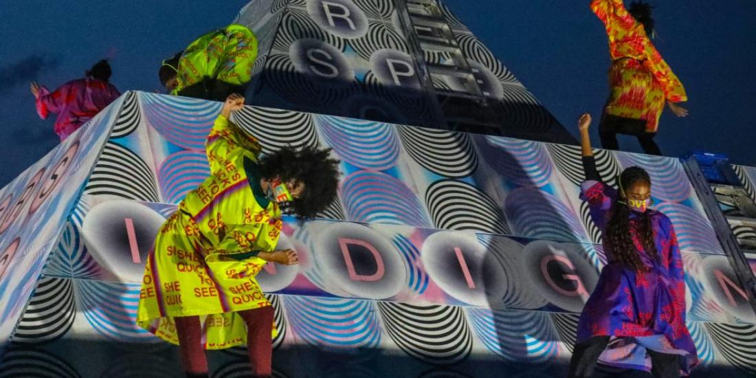 5 performers dressed in colorful neon atop Jeffrey Gibson's installation.