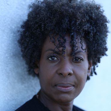 Portrait of Helga Davis in a black shirt standing against a white wall