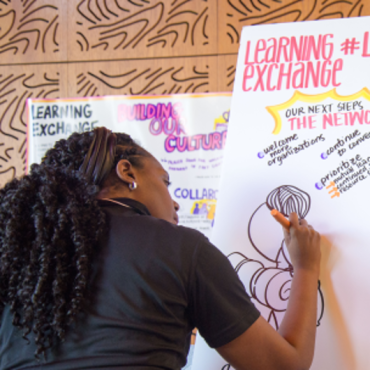 A Black woman in a black t-shirt sketching notes.