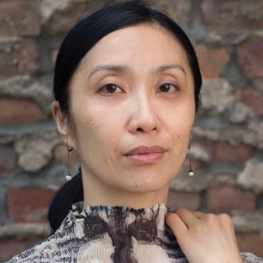 Close up portrait of Janet Wong, standing against a brick wall