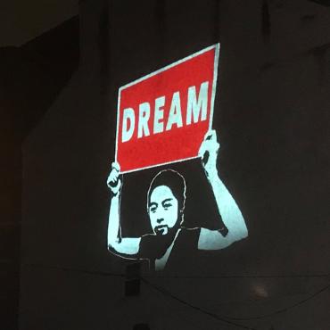 A projection on a building showing someone holding a red sign that says "Dream."